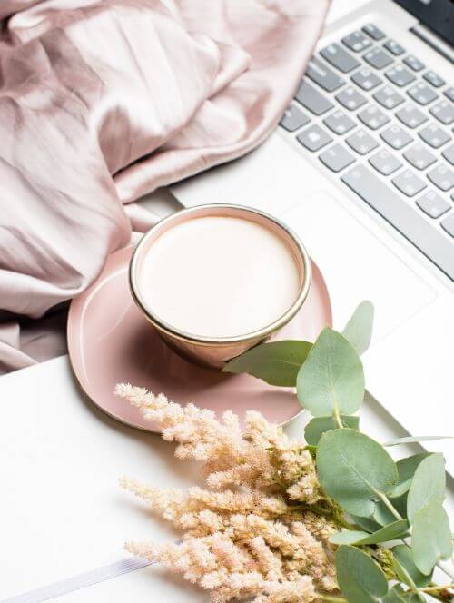 Milky coffee with dried flowers and satin cloth beside a keyboard, creating a calm workspace atmosphere